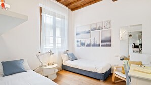 Un dormitorio con dos camas, un escritorio, una silla, una lámpara y una ventana.