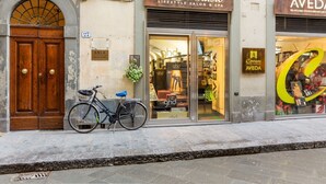Un edificio con una puerta doble de madera, una bicicleta estacionada afuera y locales comerciales con letreros que dicen 'Contrasto Lifestyle Salon & Spa' y 'Aveda'.