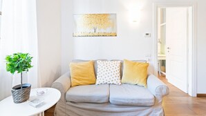 Una sala de estar con un sofá, una mesita con una planta y un cuadro en la pared.
