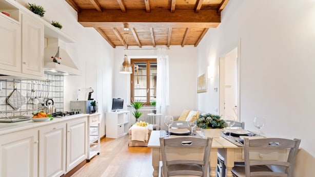 Una cocina moderna con armarios blancos, techo de madera y un comedor con dos sillas y una mesa para dos.