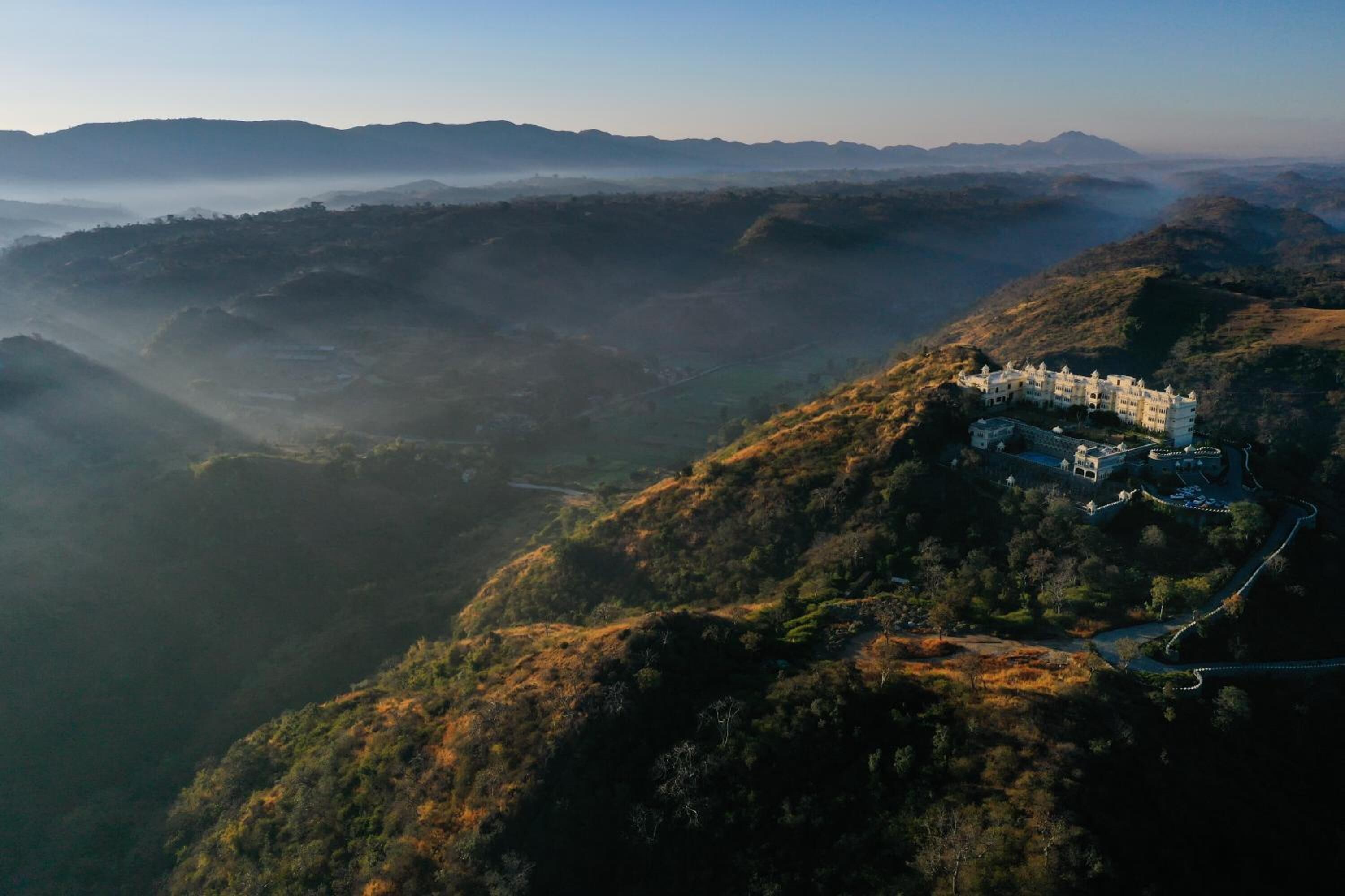 Un edificio grande e histórico con múltiples torres, ubicado en una colina con vistas a un valle.