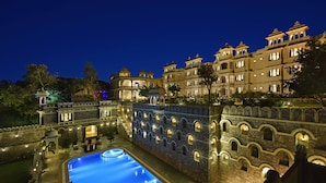 A large, illuminated swimming pool with a stone wall and arched windows, surrounded by a multi-story building with balconies and a courtyard. - The Kumbha Bagh (Kumbhalgarh)