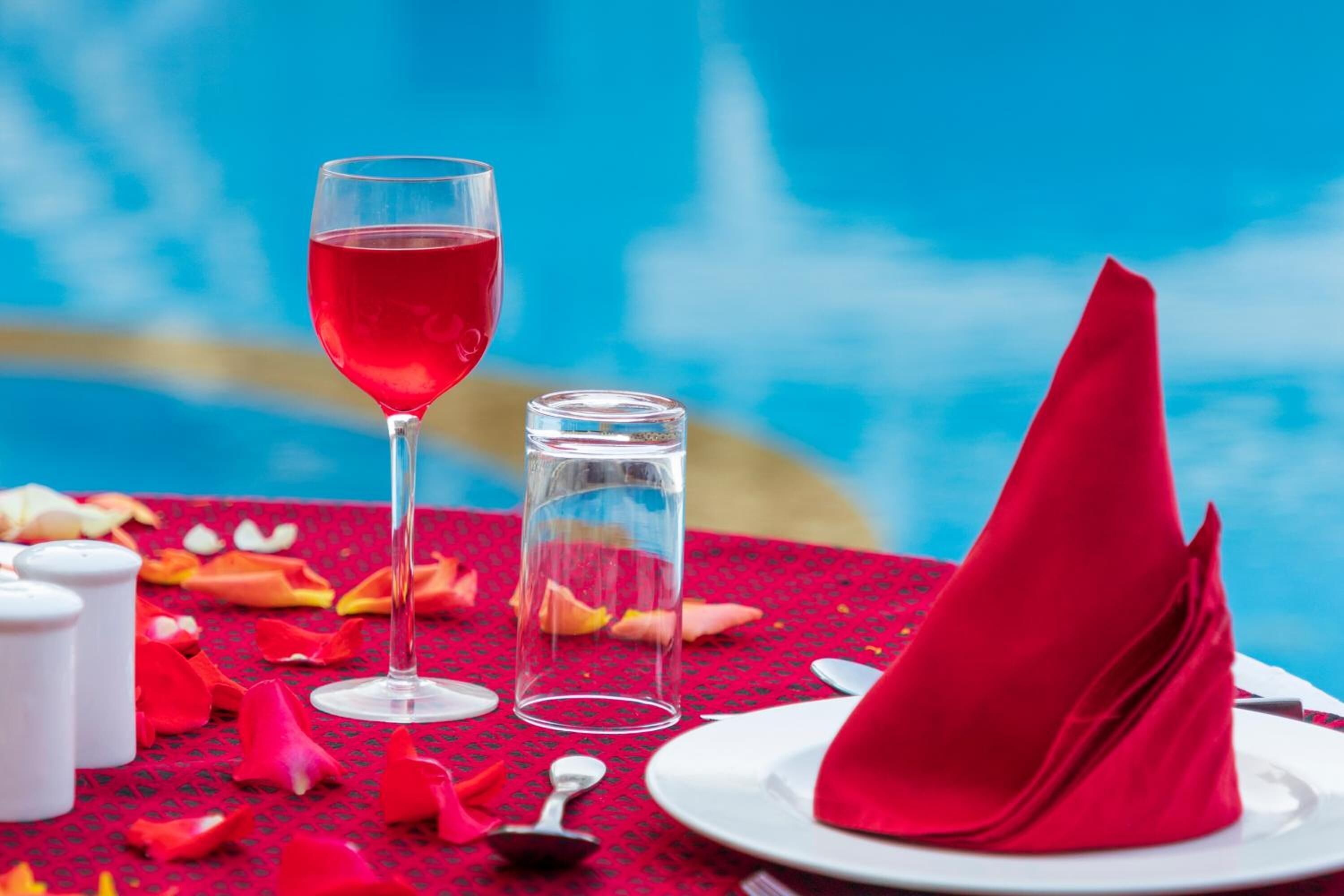 Une table dressée avec une serviette rouge, un verre contenant un liquide rouge et un verre transparent.
