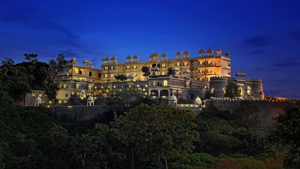A large, illuminated hotel with multiple domes and towers, surrounded by lush greenery. - The Kumbha Bagh (Kumbhalgarh)