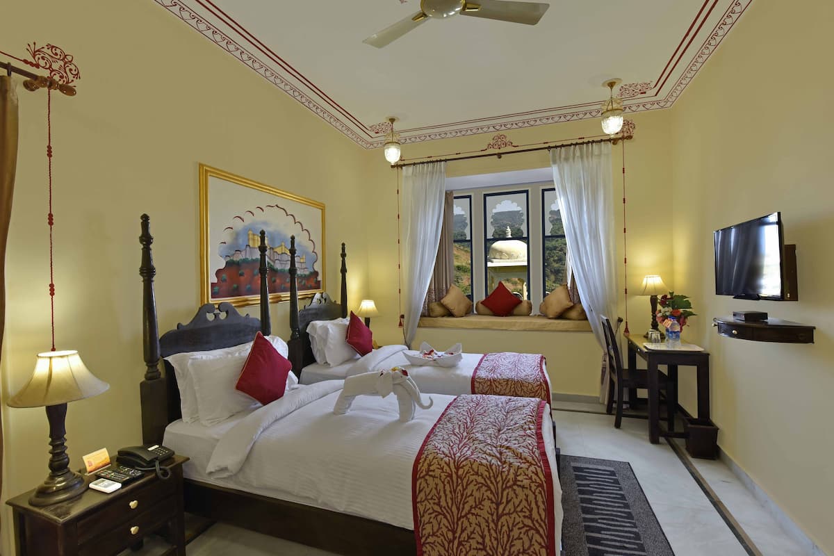 A hotel room with two beds, a desk, a television, and a window with curtains.