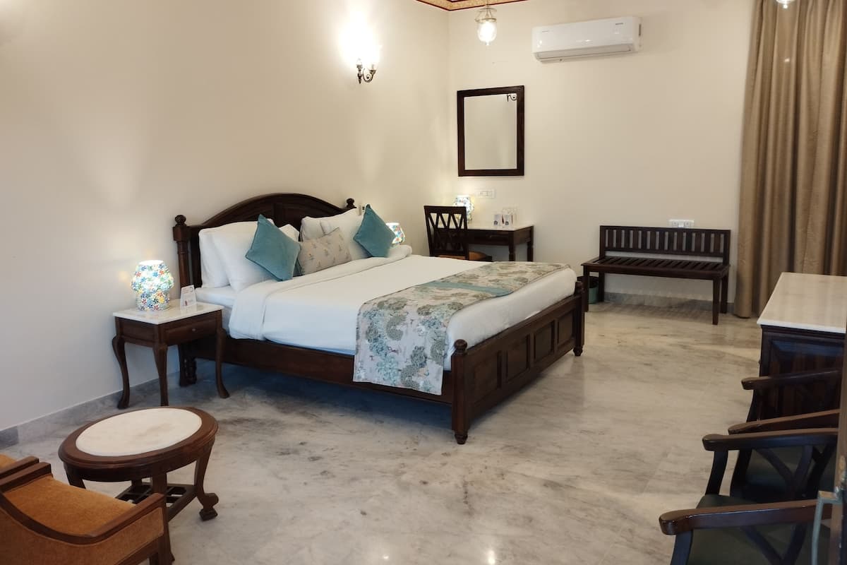 A bedroom with a bed, bedside tables, a chair, a bench, a mirror, and an air conditioning unit.