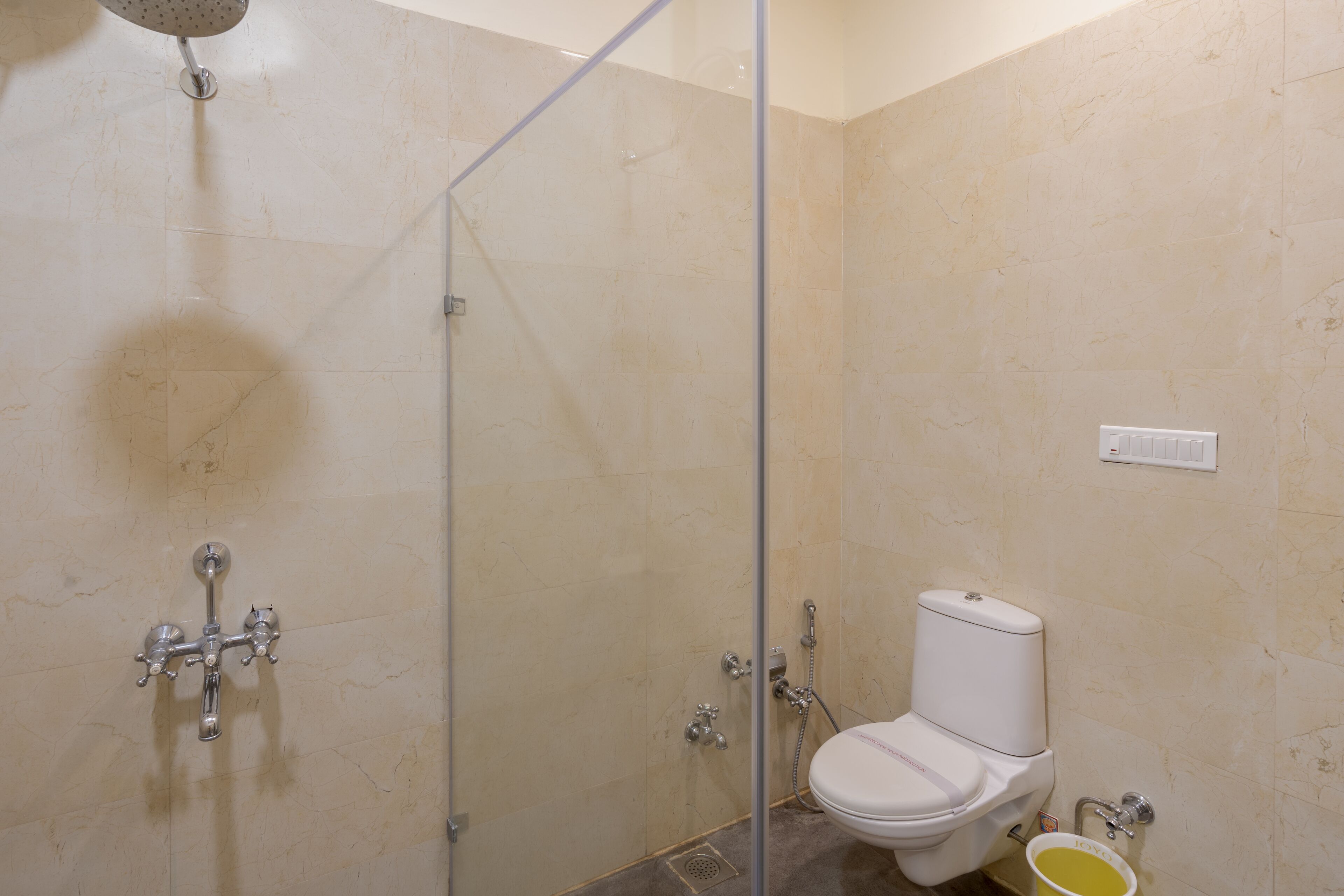Un baño con cabina de ducha de vidrio, un inodoro y un pequeño cubo amarillo.