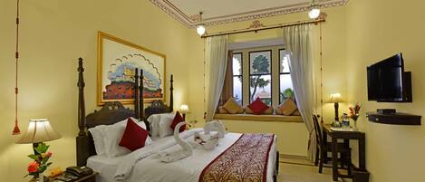 A hotel room with a bed, bedside table, lamp, TV, and a window with curtains.