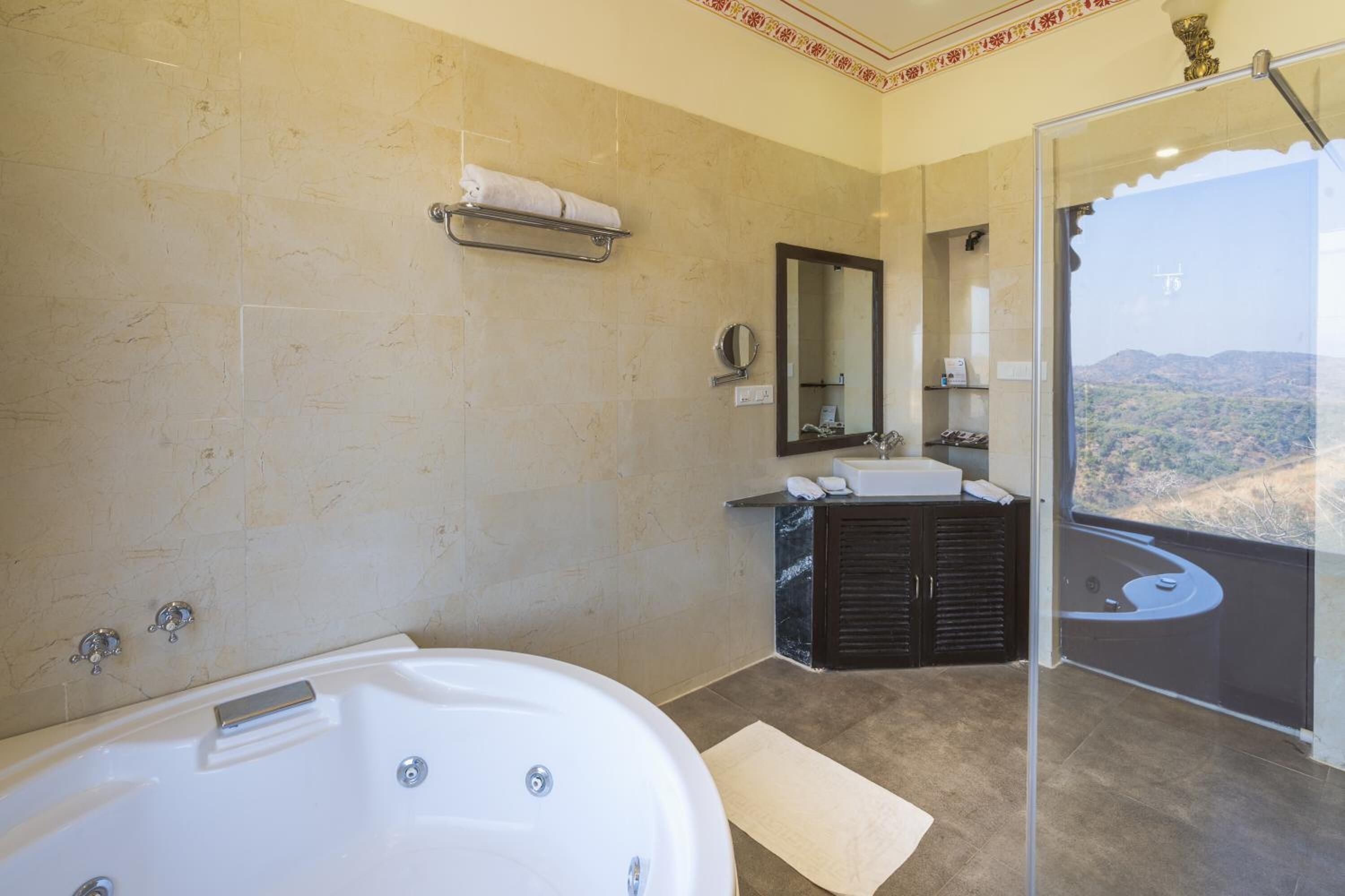A modern bathroom with a large bathtub, a vanity with a mirror, and a sink. There is a towel rack above the sink and a glass shower enclosure with a view of the mountains.