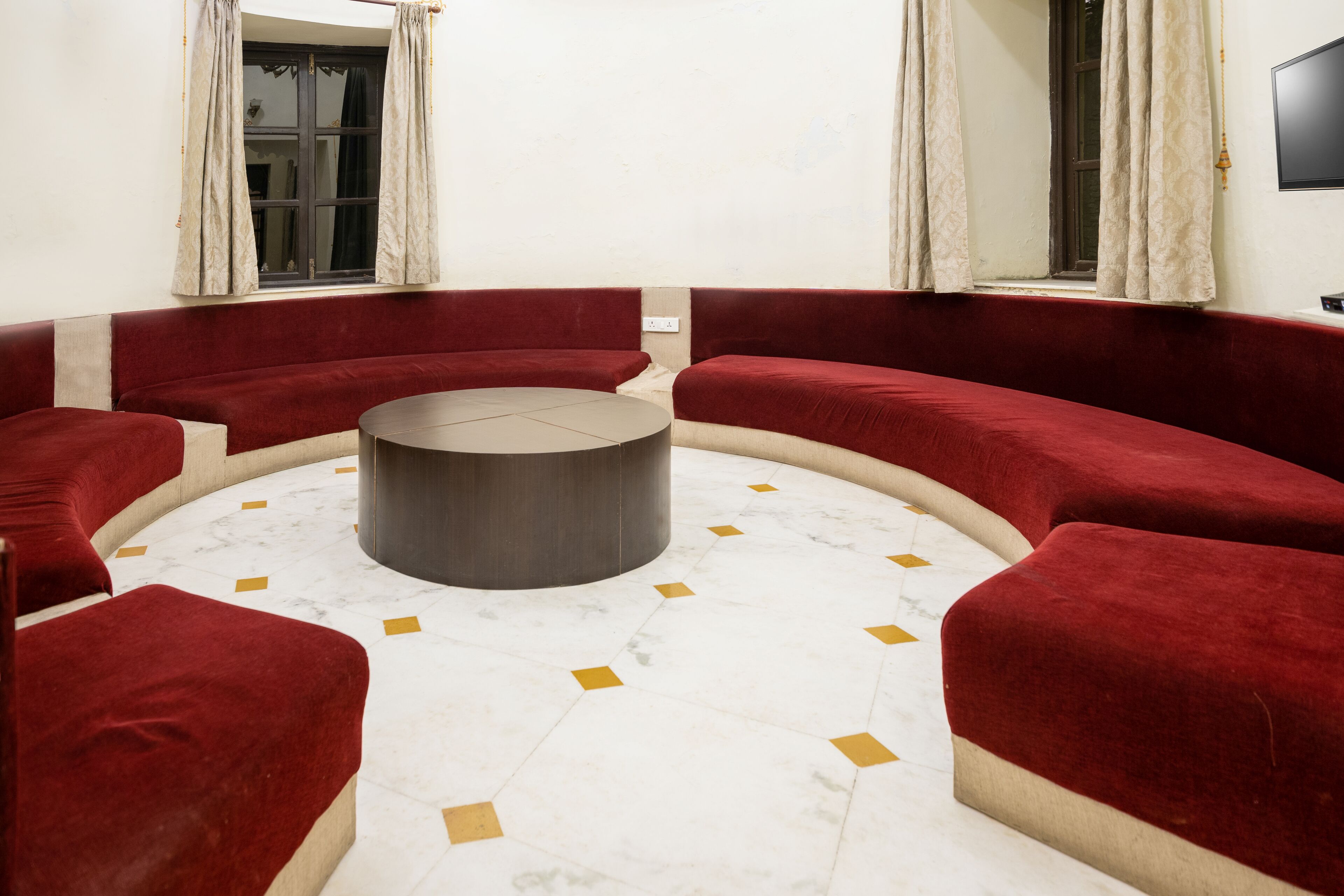 A circular seating area with a central table, surrounded by red upholstered sofas, on a marble floor with geometric patterns.