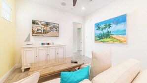 Una sala de estar con una mesa de centro de madera, un sofá color beige, cojines color turquesa, un armario blanco y dos cuadros en las paredes.