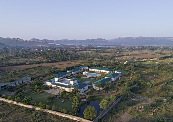 An aerial view of a large, modern hotel complex with multiple buildings, green roofs, and well-maintained lawns. - Hotel Sariska Manor (Rajgarh)