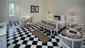 Una habitación de hotel con piso a cuadros, una cama con dos almohadas, una mesita de noche con una lámpara, una silla y una pequeña mesa con una lámpara.