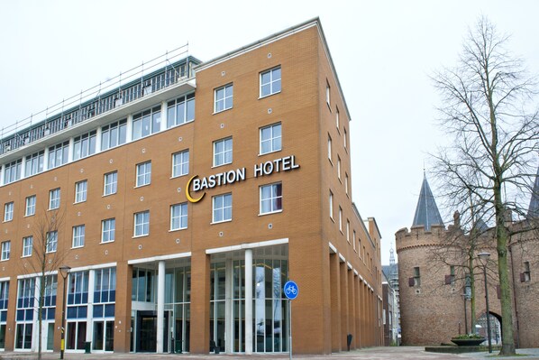 Un edificio moderno con un letrero que dice "Bastion Hotel". Tiene fachada de ladrillo, ventanas grandes y una entrada destacada.