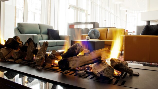 A modern hotel lobby with a fireplace, seating area, and large windows. - Bastion Hotel Arnhem (Arnhem)