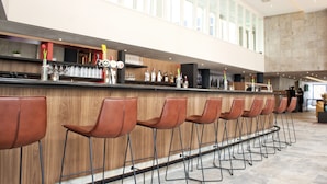 A modern bar area with a long counter, multiple stools, and a high ceiling with natural light. - Bastion Hotel Arnhem (Arnhem)