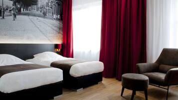 Habitación de hotel con dos camas, una silla y un ventanal grande con cortinas rojas.