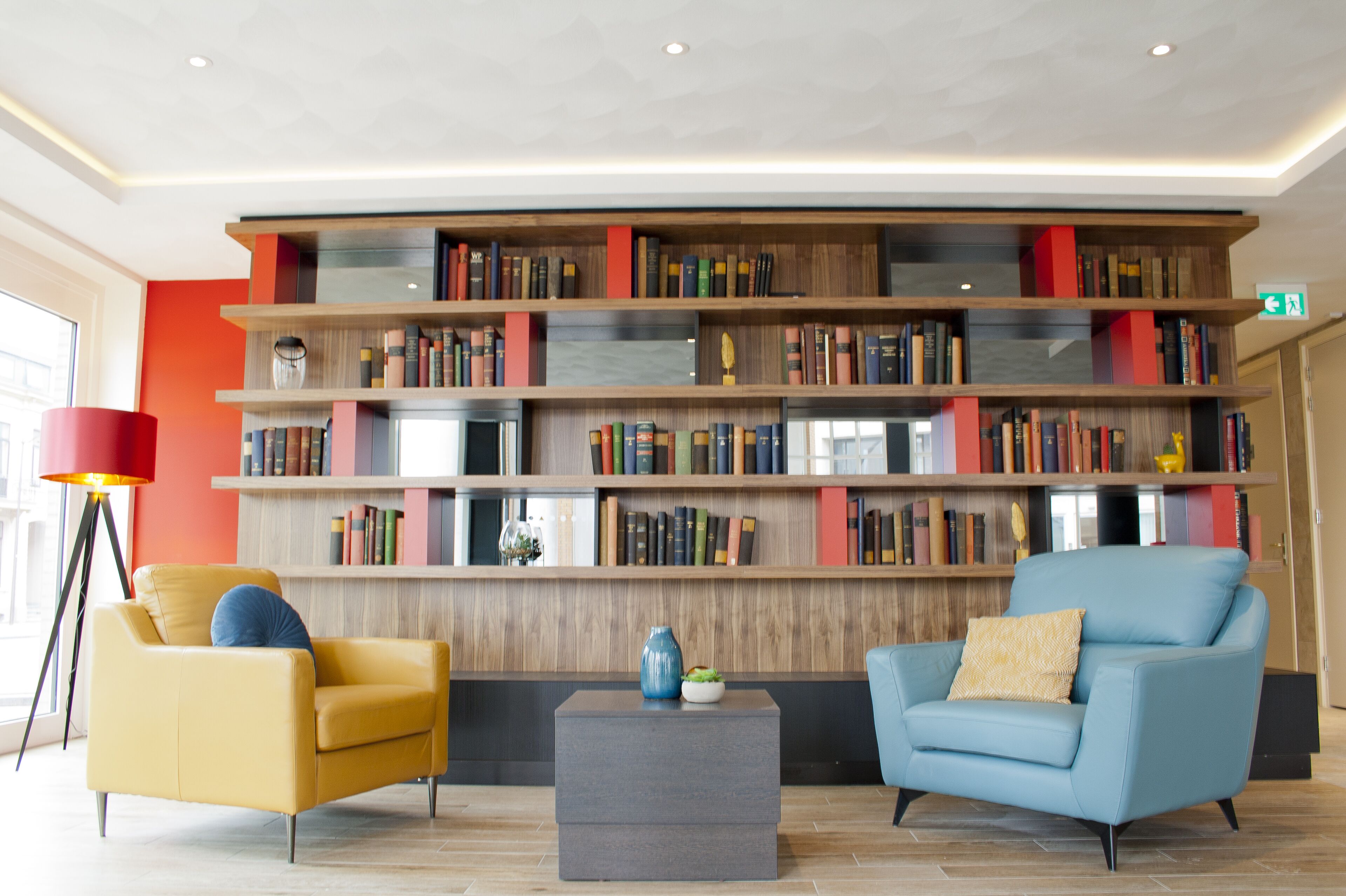 Una biblioteca moderna con dos sillones, una mesa de centro y una estantería llena de libros.