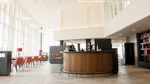 A spacious lobby with a central reception desk, seating area, and a large windowed wall. - Bastion Hotel Arnhem (Arnhem)