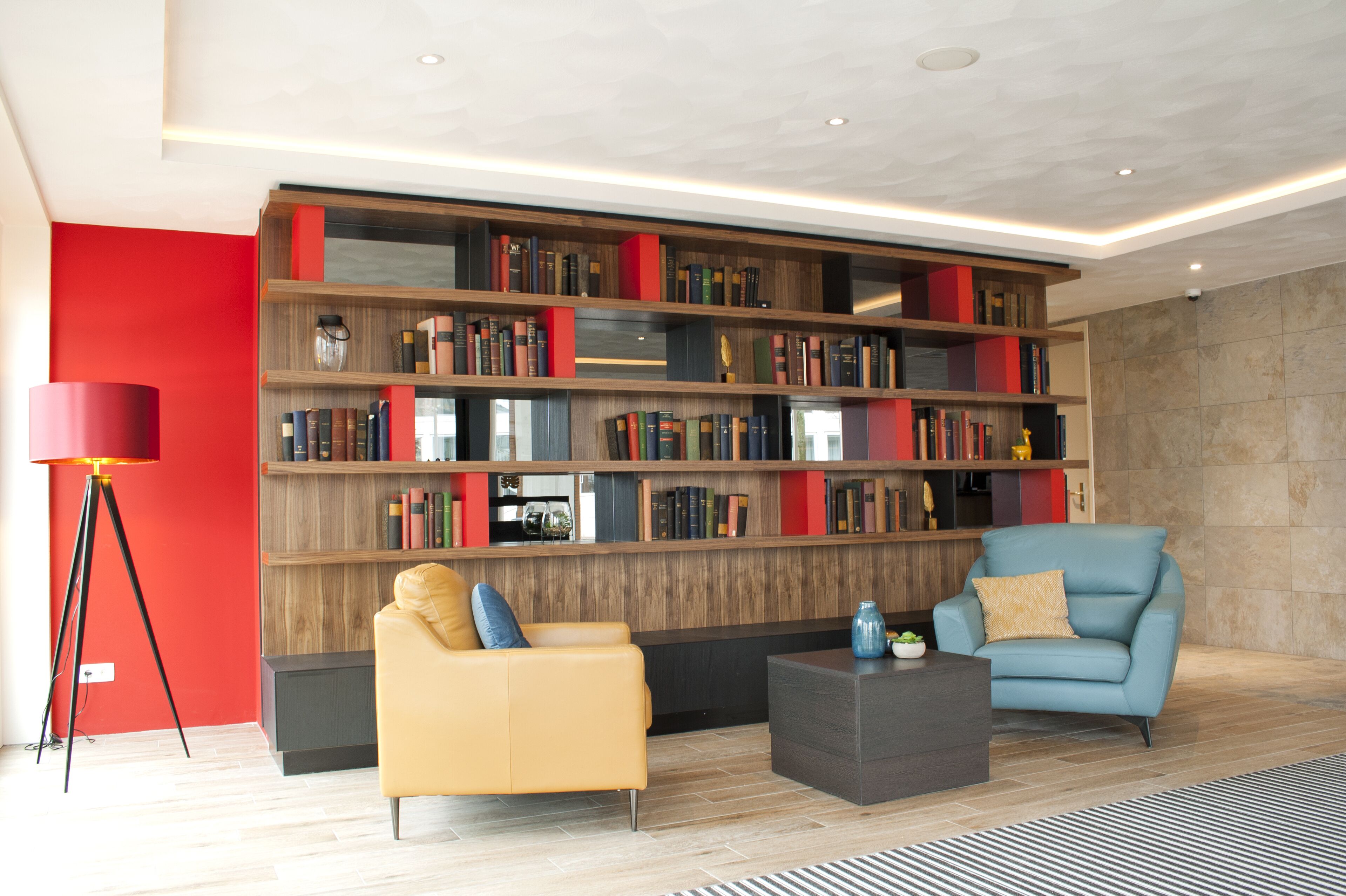 Un salon moderne avec une grande bibliothèque, un canapé jaune, un fauteuil bleu et un lampadaire.