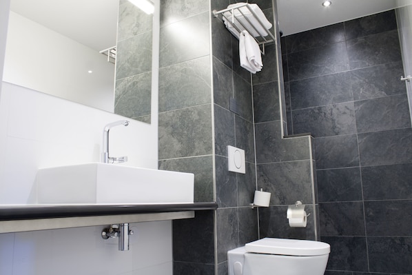 A modern bathroom with a white sink, a toilet, and dark tiled walls. - Bastion Hotel Arnhem (Arnhem)