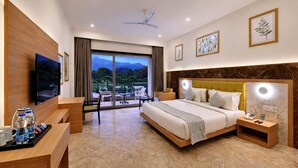 A hotel room with a bed, bedside tables, a TV, a desk with a chair, and a view of the outdoors. - Villa Le Palm - Luxury Resort Near Fateh Sagar Lake (3 KM) Udaipur (Udaipur)