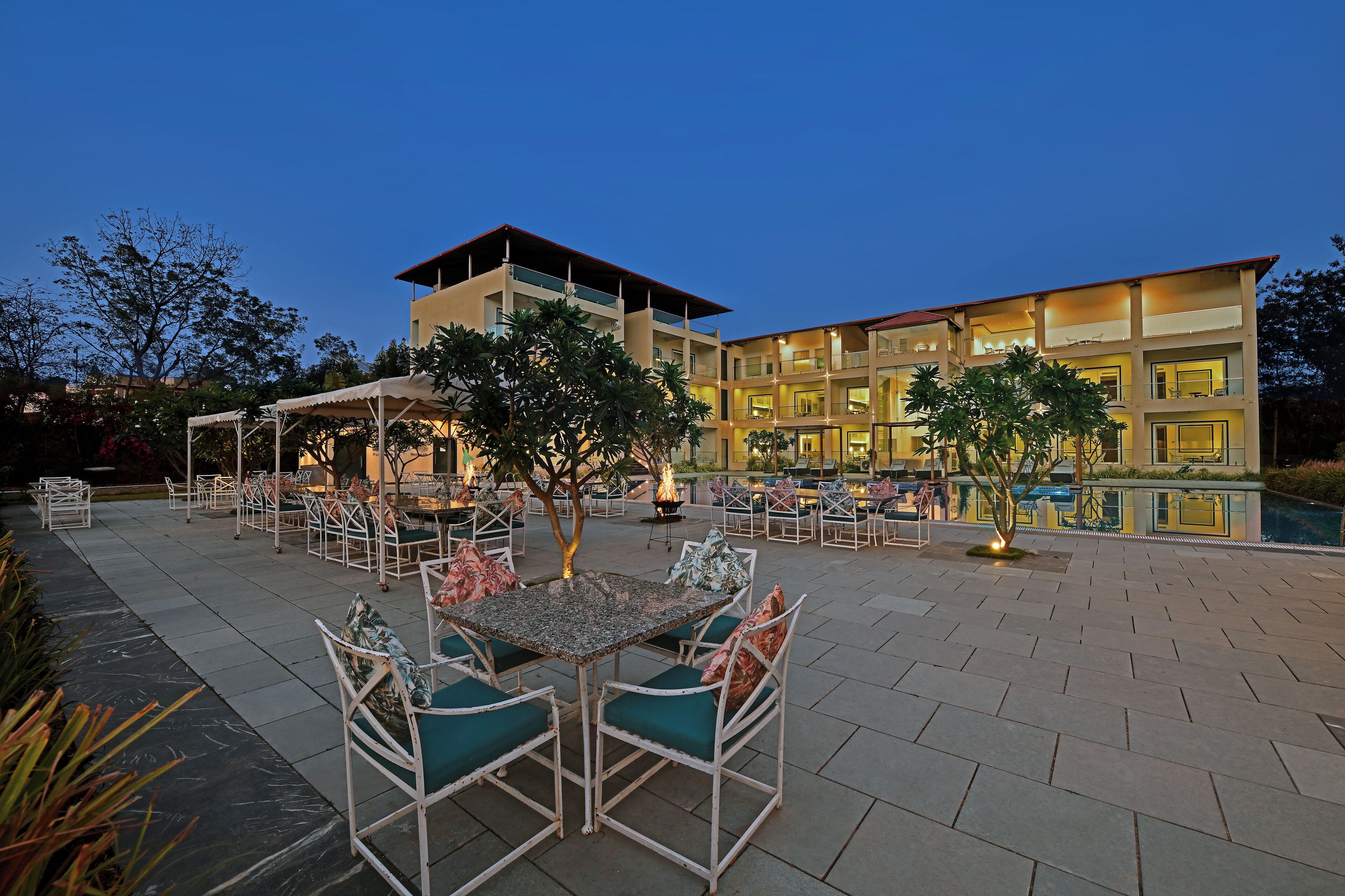 An outdoor patio area with tables and chairs, a pool, and a building with multiple floors and balconies.