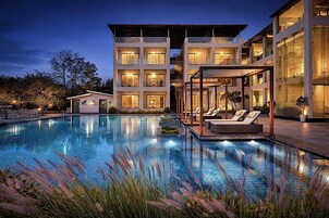 Un hotel moderno con piscina, mobiliario exterior y un edificio de varios pisos con balcones.