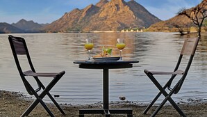 A table with two chairs by a lake with mountains in the background. - Villa Le Palm - Luxury Resort Near Fateh Sagar Lake (3 KM) Udaipur (Udaipur)