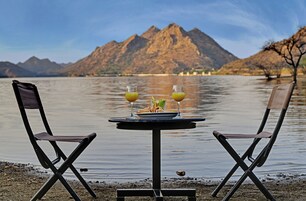 Una mesa con dos sillas junto a un lago, con montañas al fondo.