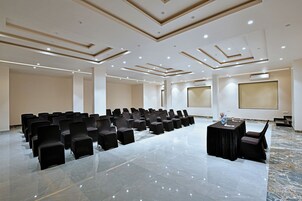 Un salón de conferencias con filas de sillas, una mesa y una pantalla para proyector.