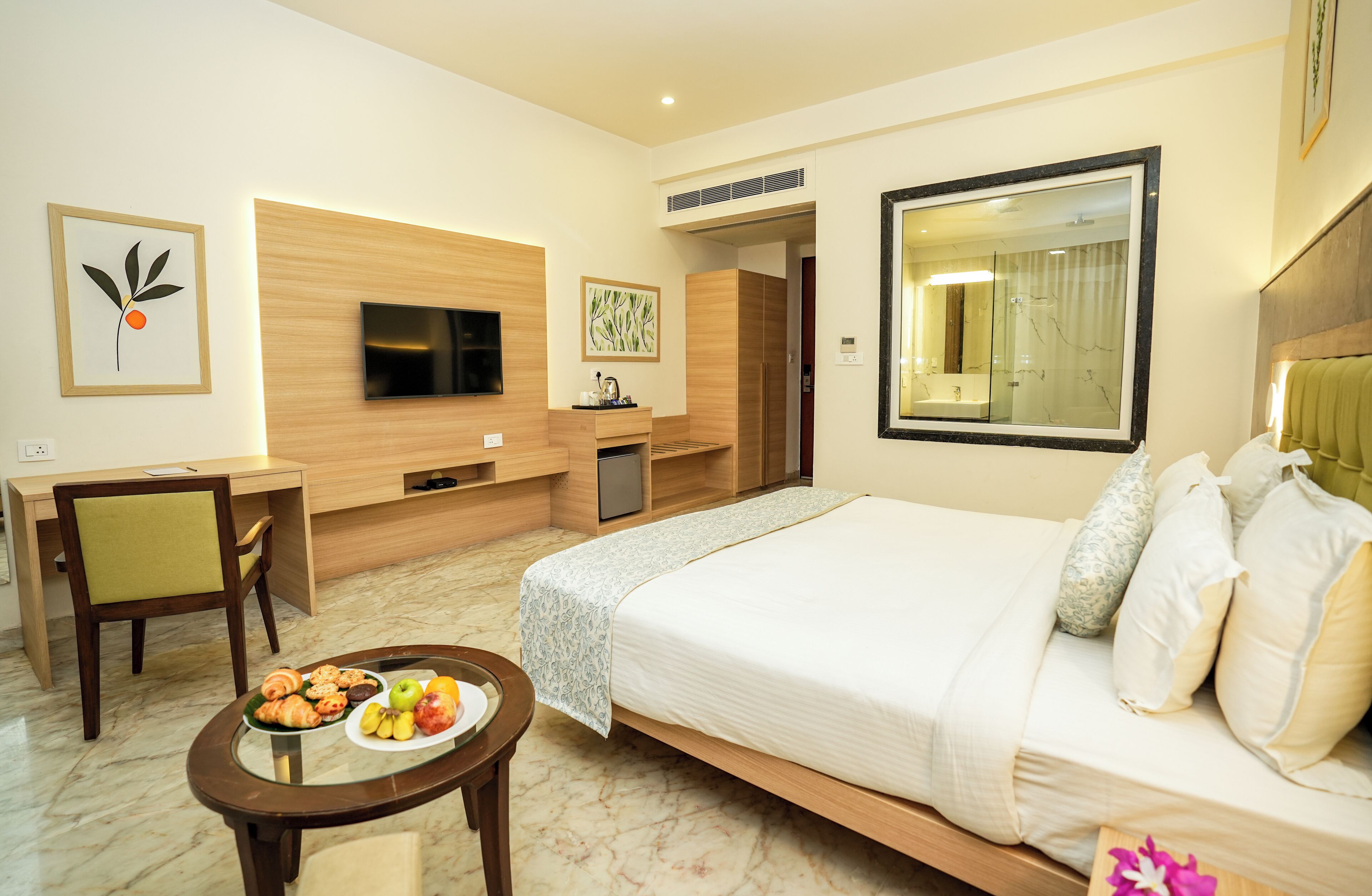 A hotel room with a bed, a desk, a chair, a TV, and a small table with food.