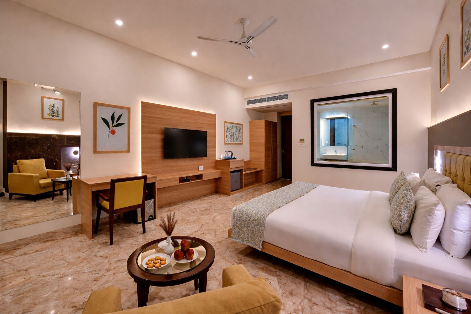 A modern hotel room with a large bed, a desk with a chair, a television, and a bathroom with a large mirror.
