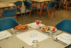 Una mesa de comedor servida con platos de comida, cubiertos y un vaso de bebida roja.