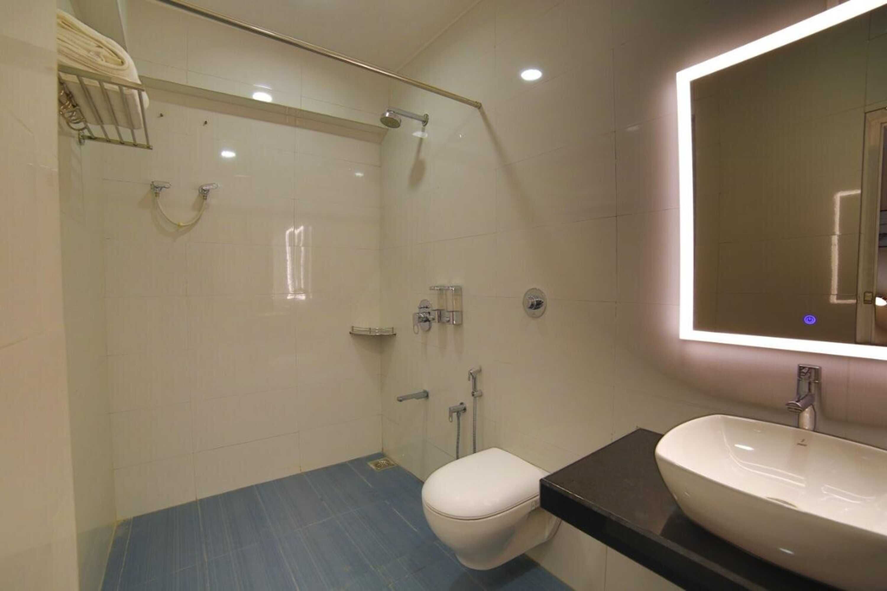 A modern bathroom with a glass-enclosed shower, a white toilet, and a large mirror with built-in lighting.