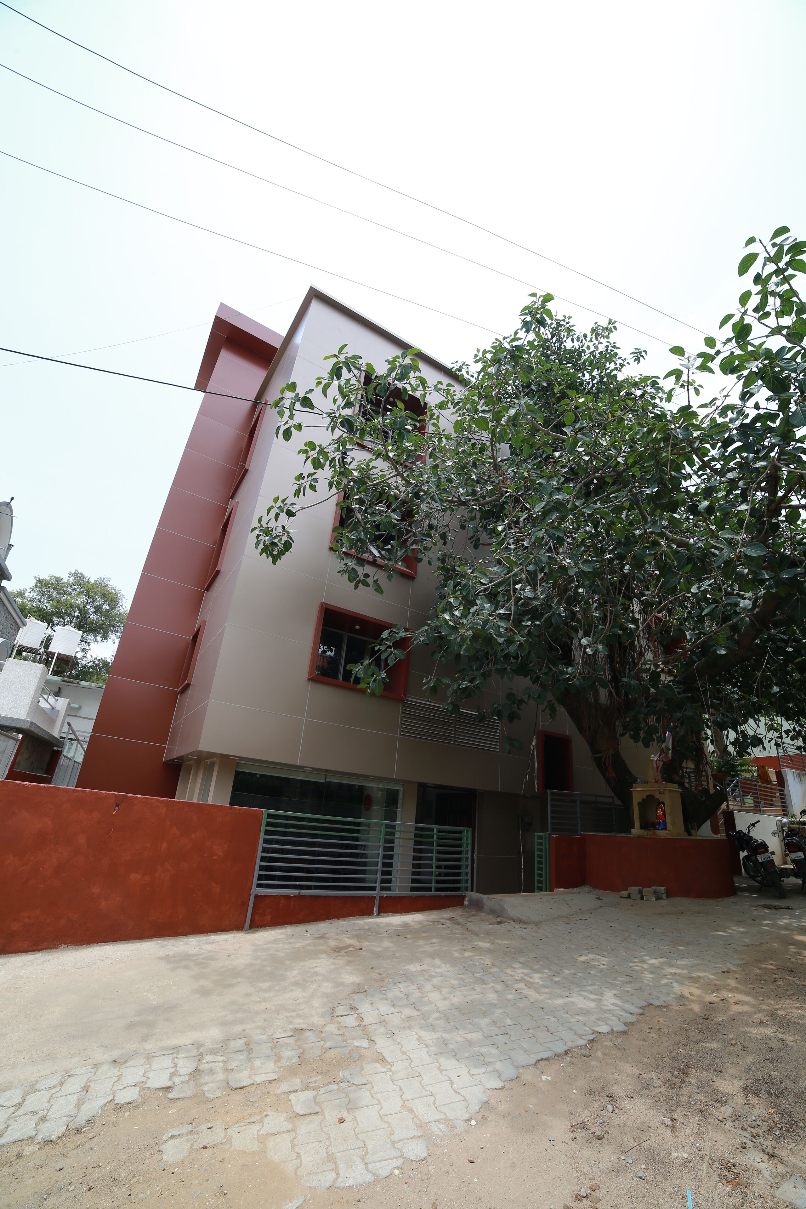 A multi-story building with a red and beige facade, a gated entrance, and a tree in front.