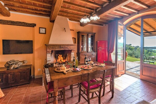 A rustic dining area with a fireplace, wooden furniture, and a view through a glass door. - Chianti Sunshine at Marioli (Bucine)