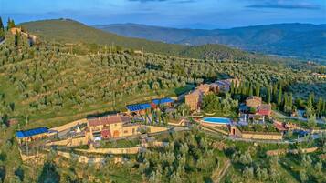 Una vista aerea di una proprietà rurale con diversi edifici, una piscina e uliveti circostanti.