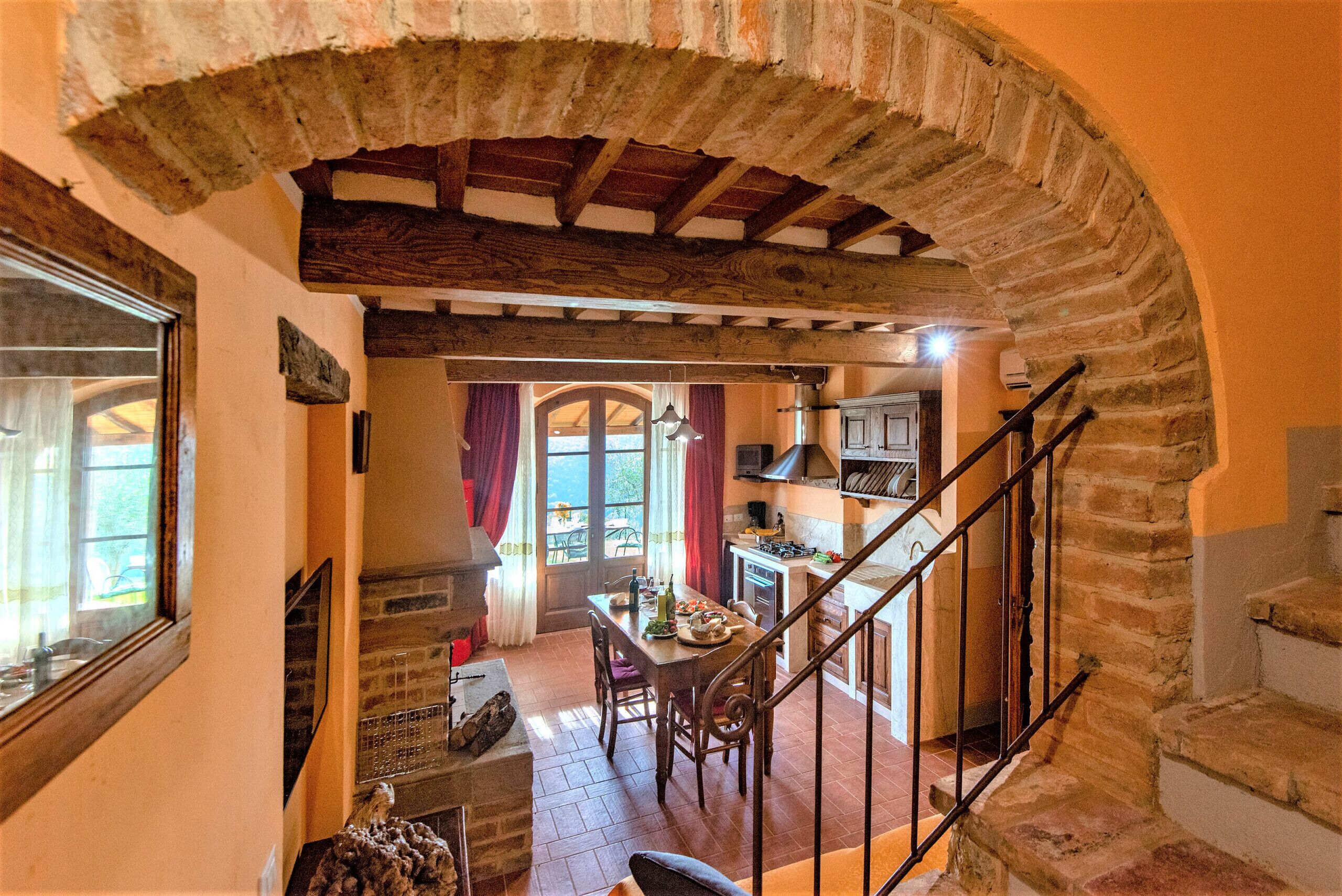 Un interno rustico con un arco in pietra, una zona pranzo con tavolo e sedie, una cucina con un fornello e una scala.