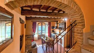 Un interno rustico con un arco in pietra, una zona pranzo con tavolo e sedie, una cucina con un fornello e una scala.