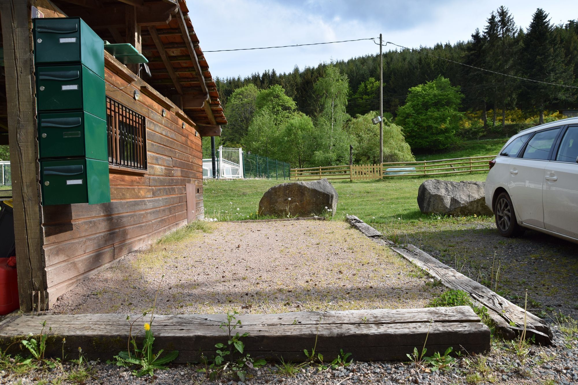 A rustic cabin with a gravel driveway and a wooden fence.