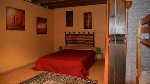 A bedroom with a wooden bed, a red bedspread, a patterned rug, and three paintings on the wall.