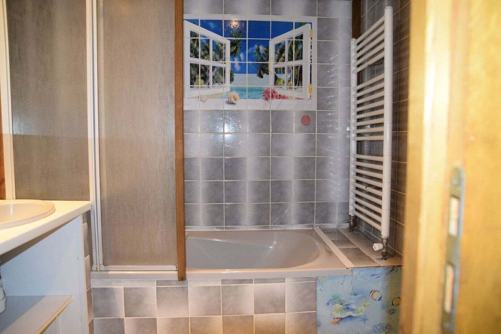 Une salle de bain avec une baignoire, une fenêtre donnant sur des palmiers et un sol carrelé.