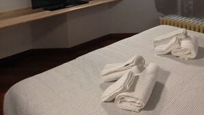 Une chambre d’hôtel avec un lit, un téléviseur posé sur une étagère, un radiateur et une fenêtre avec des rideaux.