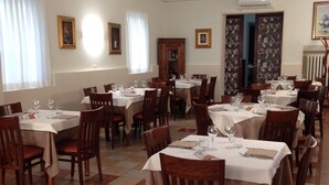 Un espace repas avec plusieurs tables dressées pour les repas, des chaises et des œuvres d’art encadrées accrochées aux murs.
