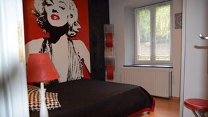 Un dormitorio con una cama, una lámpara roja, una ventana y una pared con un mural rojo y blanco.