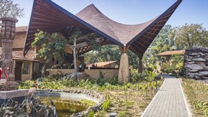 A modern building with a unique roof structure, a paved pathway, and a small pond with birds. - Serendipity Lakes and Resorts (Tamia)