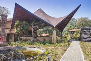 Un edificio moderno con una estructura de techo singular, un sendero pavimentado y un pequeño estanque con aves.