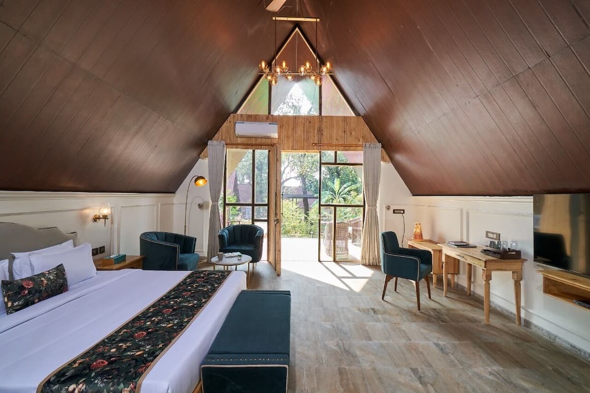 A room with a sloped ceiling, a bed with a floral bedspread, two chairs, a small table, and a television.