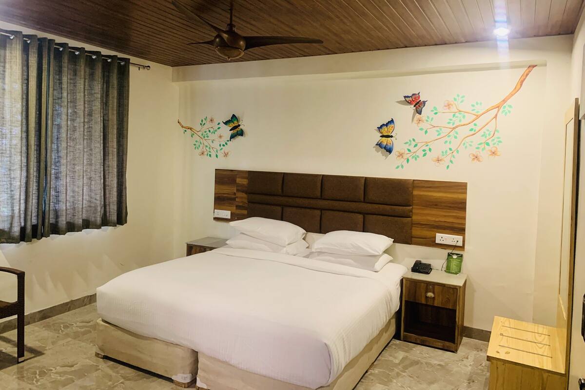 A bedroom with a large bed, wooden headboard, a ceiling fan, decorative wall art, a bedside table with a phone and a green container, and a wooden nightstand.